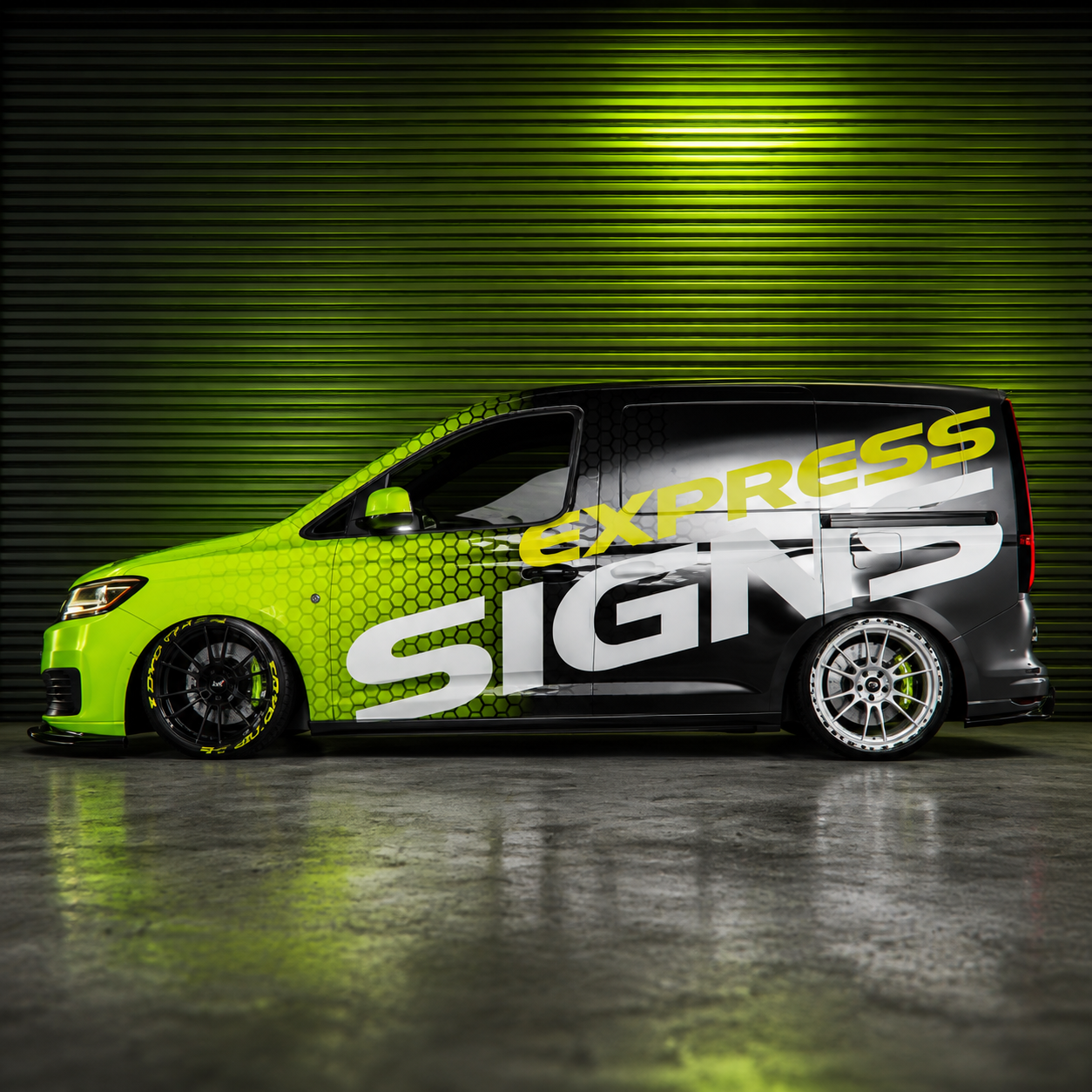 Black van with neon green geometric wrap design inside a modern vehicle wrap studio